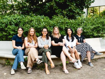 six women sitting on a bench under a tree (the Montreal FLOW team)
