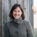 a smiling woman standing in front of a wooden barn wall