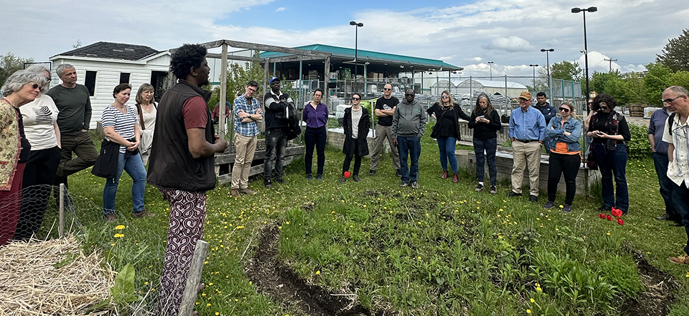 many people standing in a circle at an urban farm listening to a speaker
