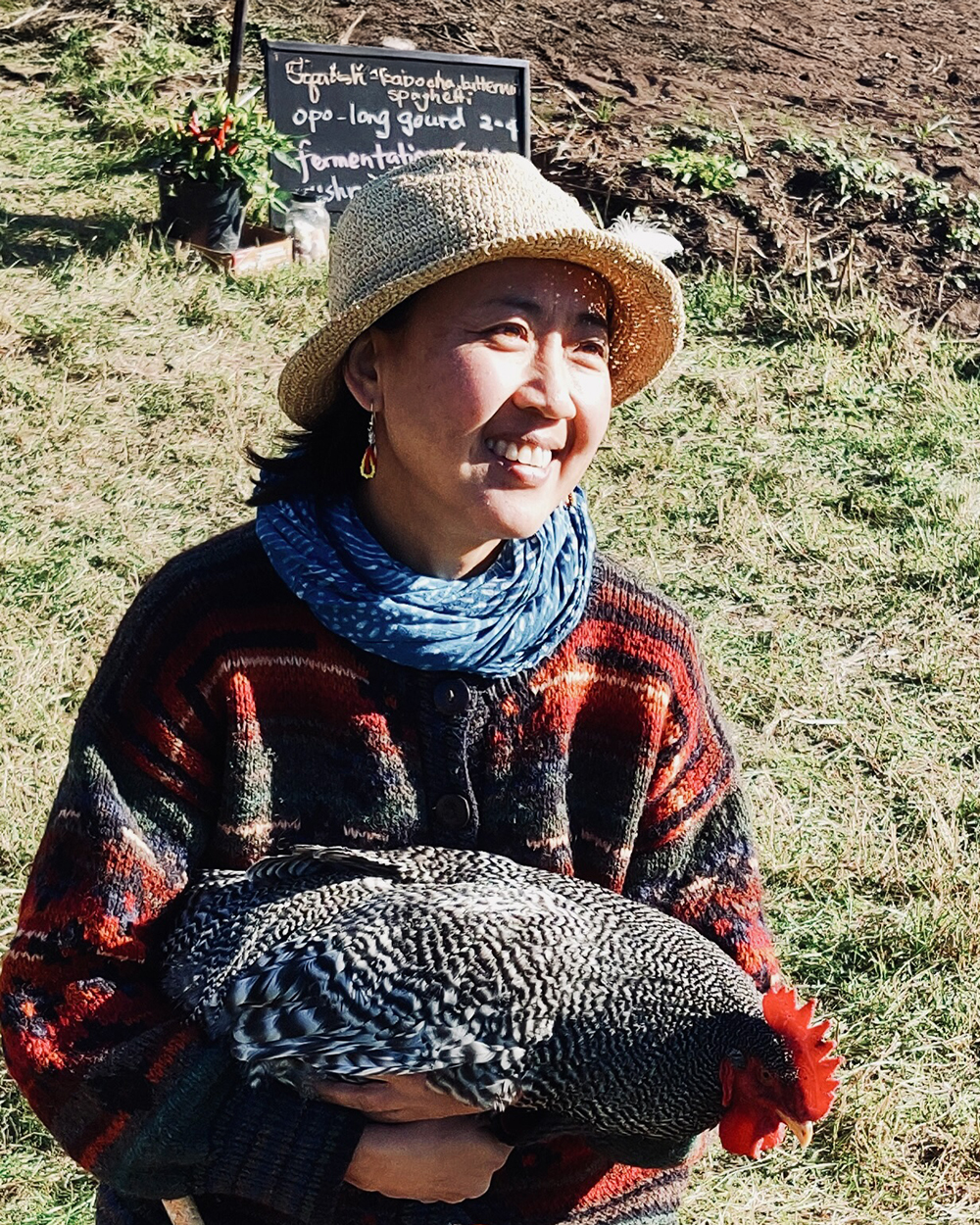 woman wearing a hat kneeling in a farm field holding a black-and-white chicken