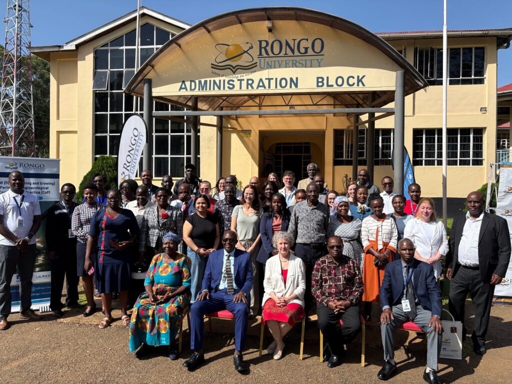 About 35 people sitting and standing in front of an institutional building with the words Rongo University Administration Block on an archway over the entrance.